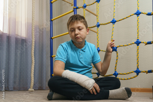 Sad child with a broken arm in the home environment . The cast on the hand of a little boy.