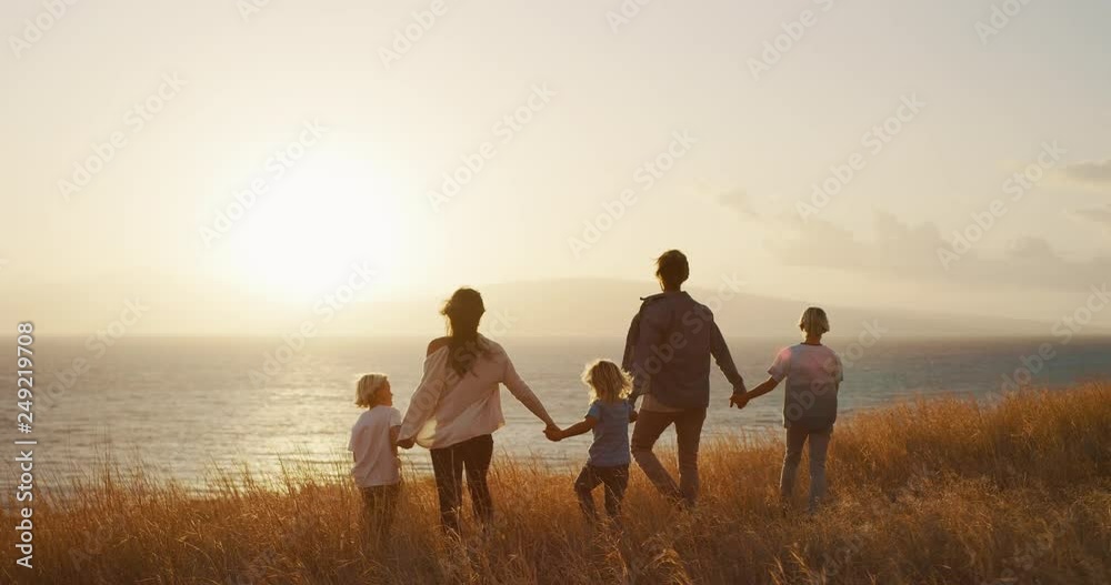 Happy family walking in golden field and looking out to the sunset together by the ocean