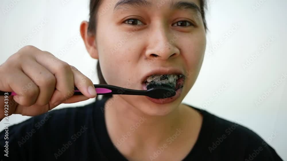 Asian young woman brushing her teeth with black toothpaste of activated charcoal, and black tooth brush on white background. Asian young woman brushing her teeth with black toothpaste of activated charcoal, and black tooth brush on white background.
