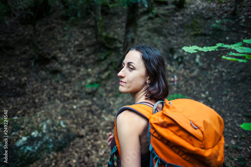 The girl with a backpack is walking through the forest.
