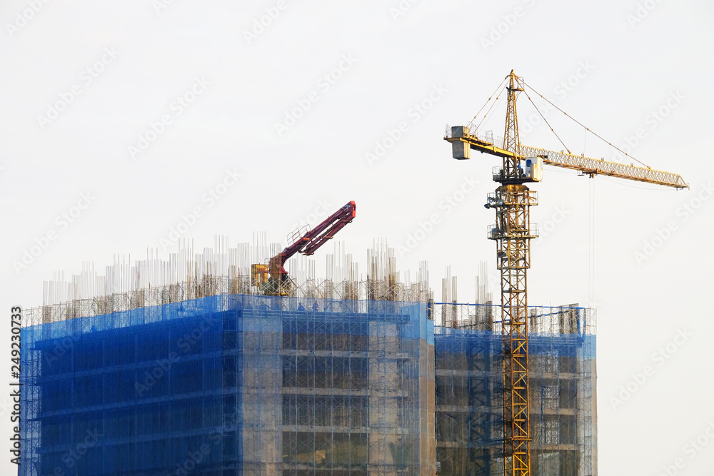 Top of big under construction building of concrete and steel structure with yellow crane and excavator truck on white sky background Top of big under construction building of concrete and steel structure with yellow crane and excavator truck on white sky background