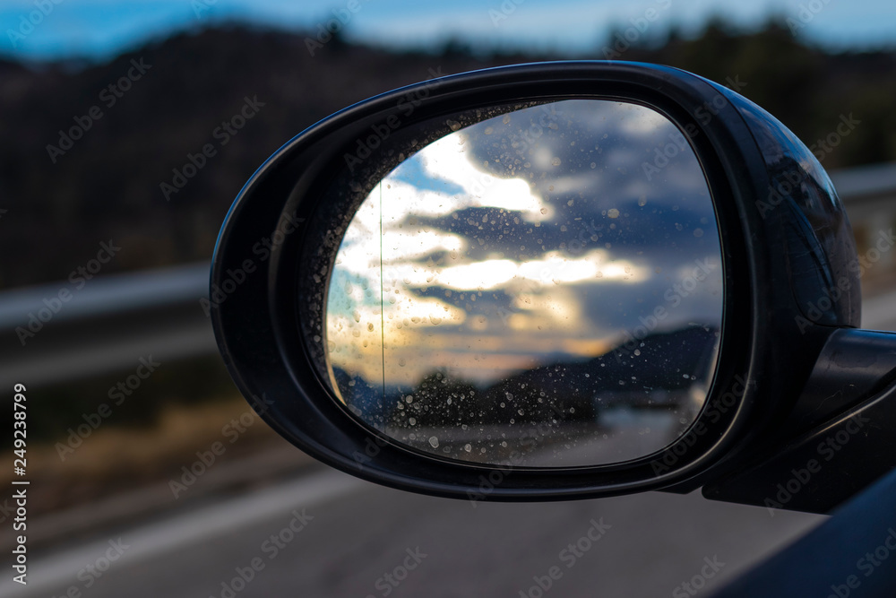 Bright cloudscape reflecting on an oval black mirror car while driving on a highway Bright cloudscape reflecting on an oval black mirror car while driving on a highway