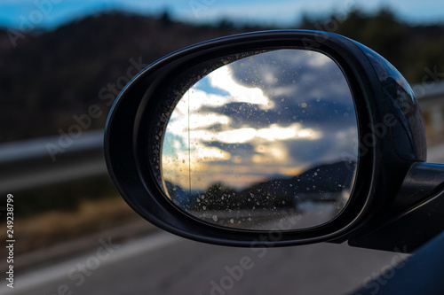Bright cloudscape reflecting on an oval black mirror car while driving on a highway