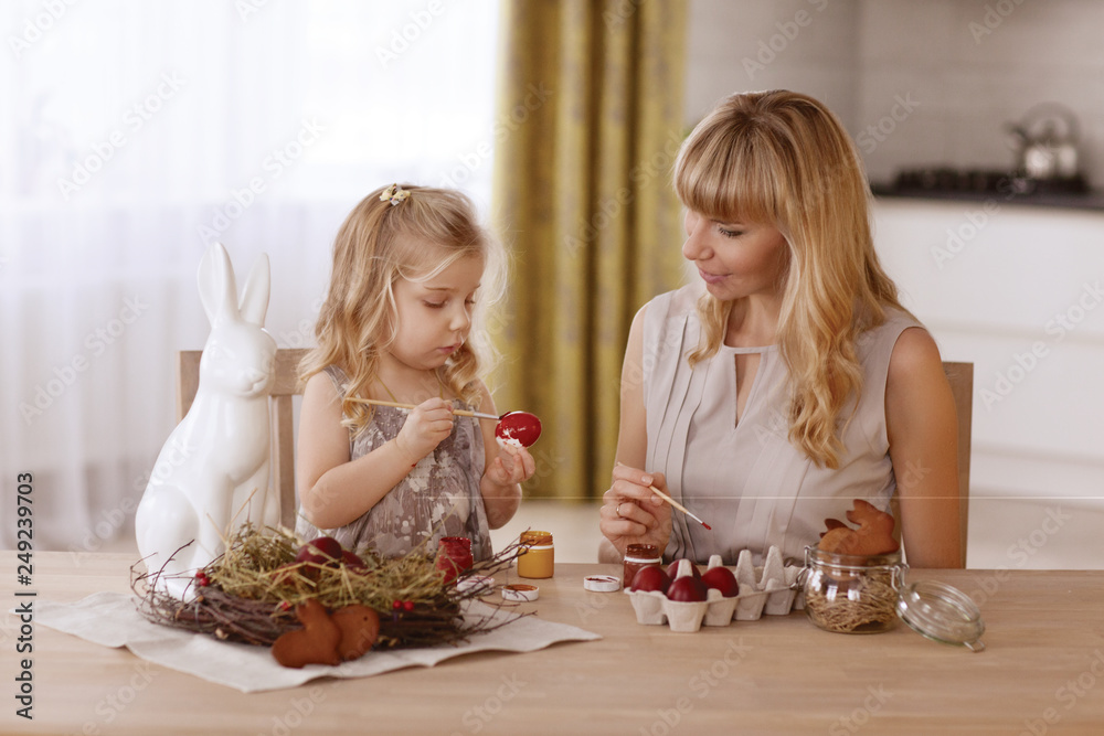 Mother and daughter paint Easter eggs in the room at the holiday table. Mother and daughter paint Easter eggs in the room at the holiday table.