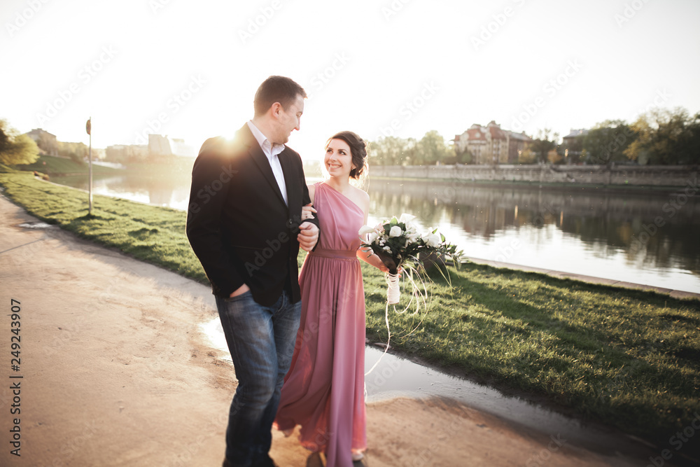 Wedding couple, groom and dress posing near river with a glass at sunset