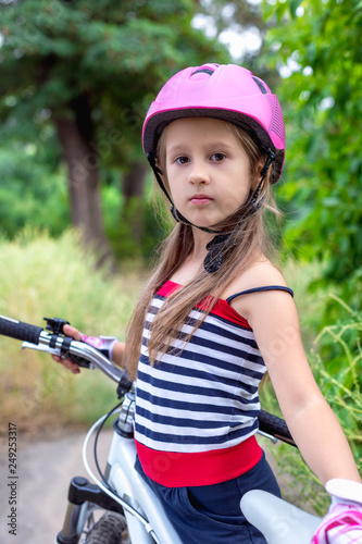 Little cute girl in a pink helmet near a bicycle