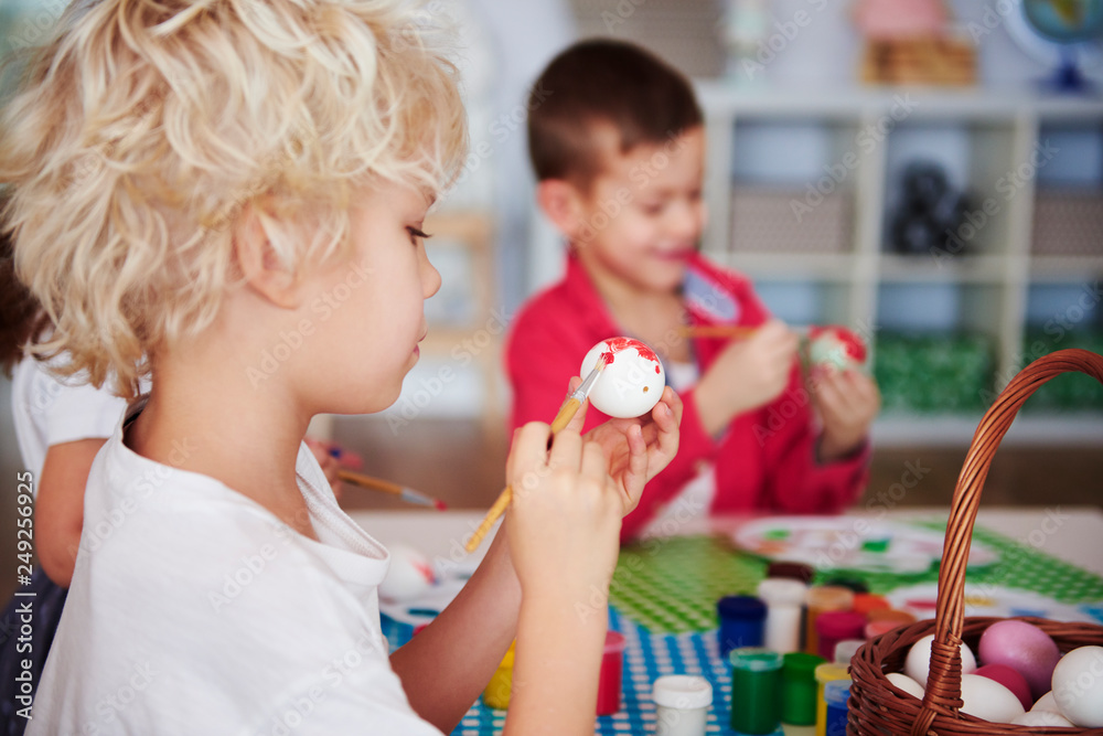 Obraz premium Side view of focused boy painting easter egg
