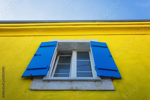 window with blue shutters over yellow wall