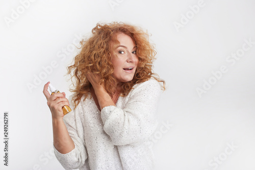 Anti-ageing Concept: Woman In Her Forties caring for curly hair, applying spray on curly red hair