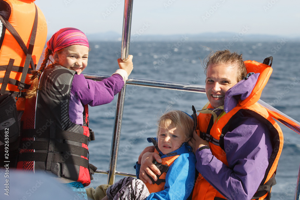 Family on a blue whale watching trip. Smiling girl in safety jacket on a boat trip. Mother holding baby..