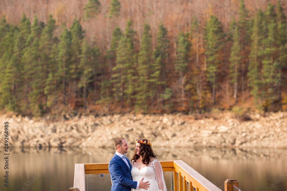 Beautiful wedding couple posing on dock near lake and forest