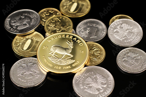 A close up image of a gold South African krugerrand with Russian Federation coins on a reflective black background photo