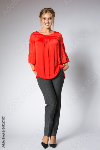 Beautiful blonde model posing in red blouse and gray pants
