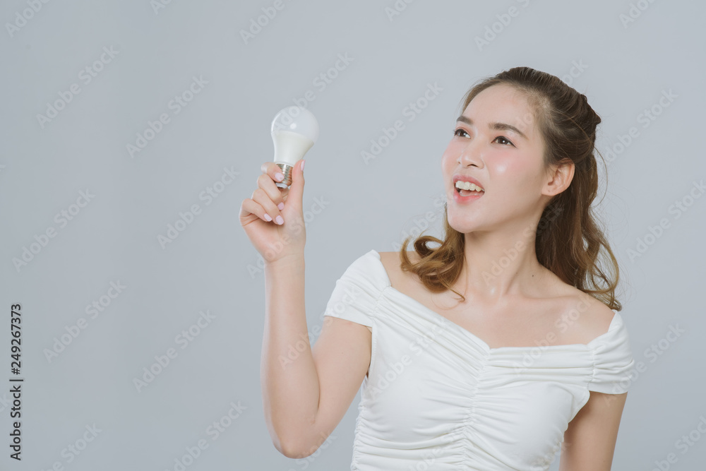 Portrait of beautiful young asian business woman smiling and holding shiny light bulb, isolated on grey background. Idea concept Portrait of beautiful young asian business woman smiling and holding shiny light bulb, isolated on grey background. Idea concept