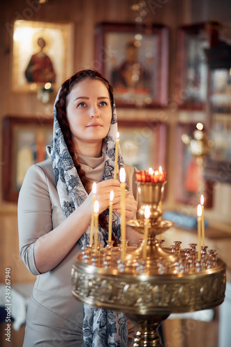 Картината върху платно woman in the Russian Orthodox Church with red hair and a scarf on her head lights a candle and prays in front of the icon