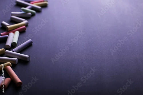 Multicolored crayons lie on a black chalkboard, copy space. The concept of school, education and childhood.
