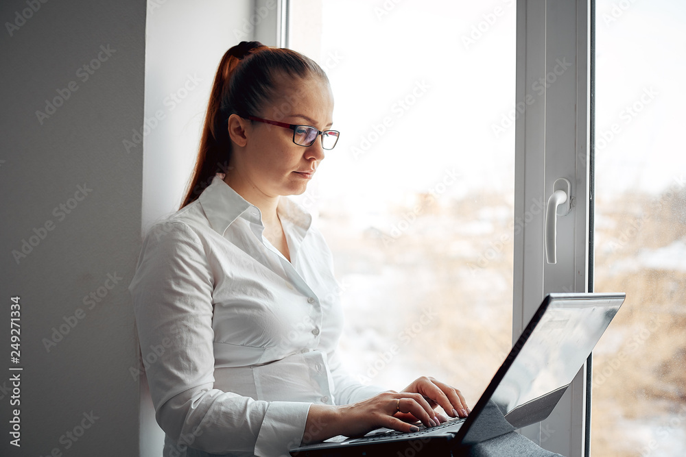 female Manager sitting on the windowsill working in the office on a laptop female Manager sitting on the windowsill working in the office on a laptop