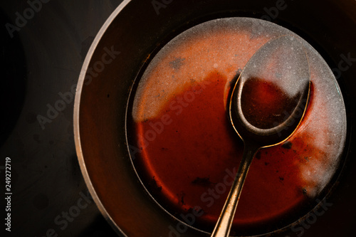 view into the pot with a spoon while cooking a morel sauce of beef stock and port wine, dark background with copy space