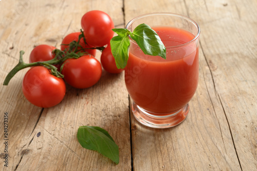 fresh tomato juice in a drinking glass with basil garnish on a rustic wooden board, healthy smoothie drink with copy space