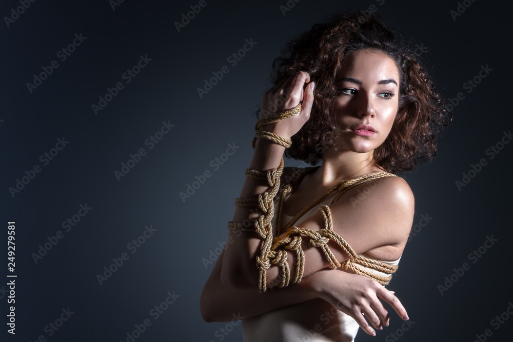 Beautiful fashion brunette woman with tied chest and hand with decorative knots of natural jute ropes. Ancient Japanese art of aesthetic bandage and tying shibari kinbaku. Sexual underwear concept.