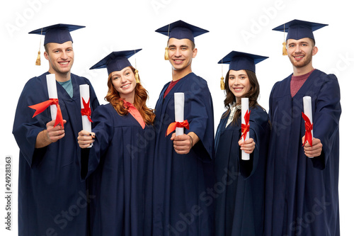 education, graduation and people concept - group of happy graduate students in mortar boards and bachelor gowns with diplomas over white background