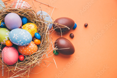 Photography Colorful easter eggs with chocolate and candies in a nest on a orange background