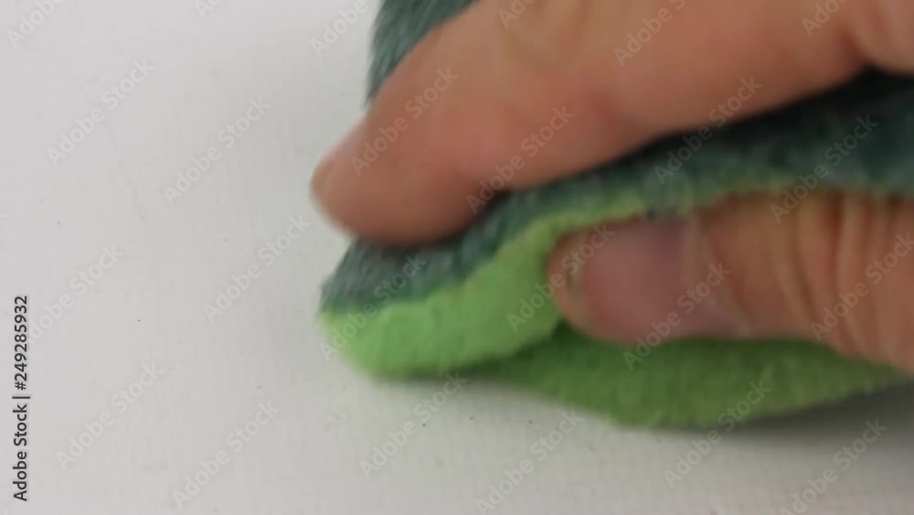human hand carefully wipes the white surface of the table with a green dish washing sponge, closeup human hand carefully wipes the white surface of the table with a green dish washing sponge, closeup