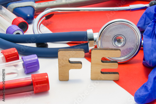 FE medical abbreviation meaning total iron or ferrum in blood in laboratory diagnostics on red background. Chemical name of FE is surrounded by medical laboratory test tubes with blood, stethoscope photo