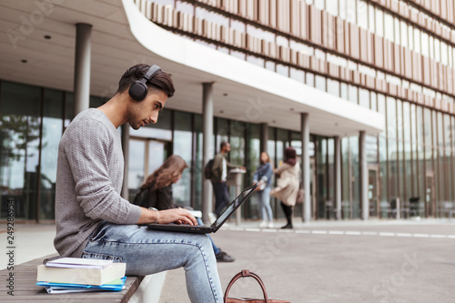 Young student listening music while using laptop at university campus photo