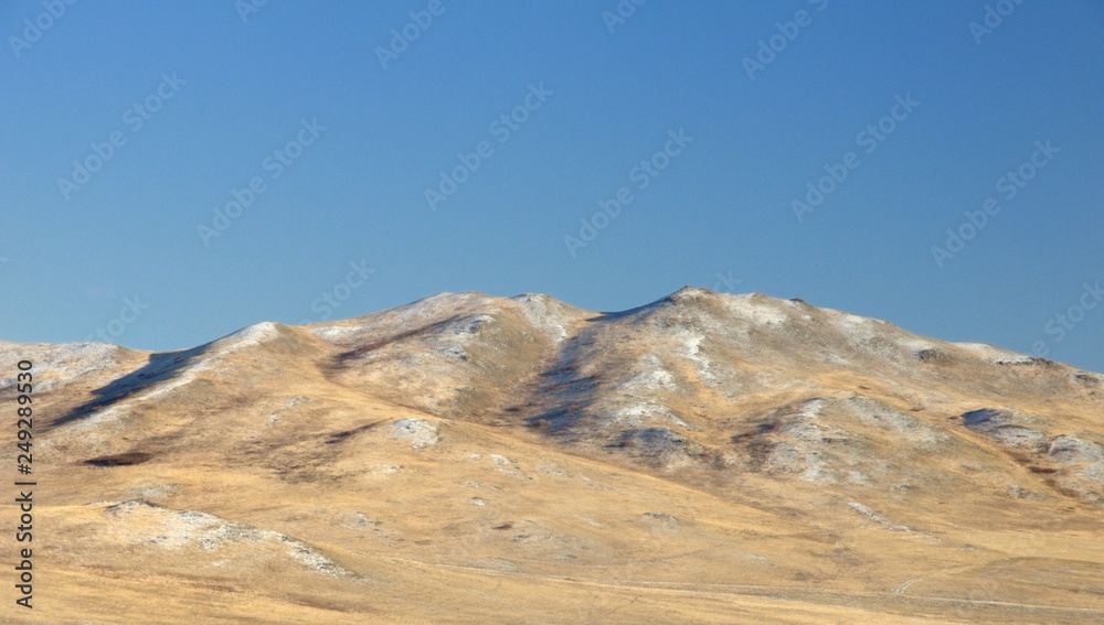 Winter landscape with a smooth hills covered with a yellow dry grass and first snow under dark blue sky in Khakassia, Russia