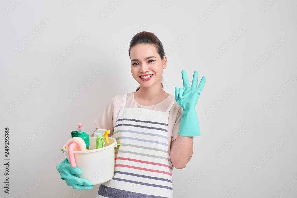 Young woman as a cleaning maid holding bucket full of liquids and showing OK sign, isolated over white Young woman as a cleaning maid holding bucket full of liquids and showing OK sign, isolated over white