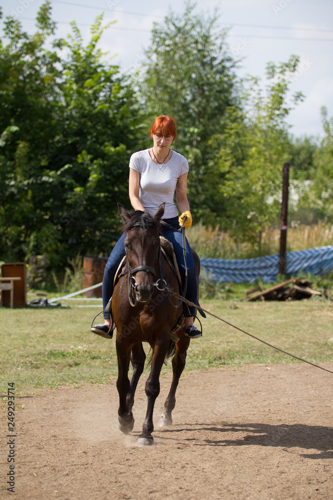 A redhead woman riding a horse on the field. A redhead woman riding a horse on the field.