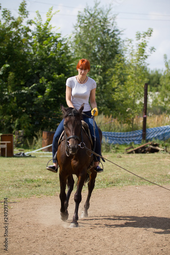 A redhead woman riding a horse on the field.