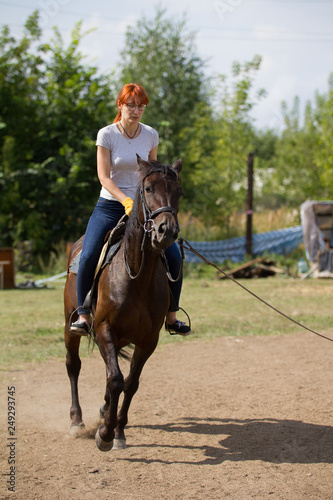 A redhead woman riding a dark brown horse on the field.