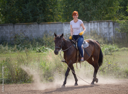 A redhead smiling woman riding a dark horse on the field.