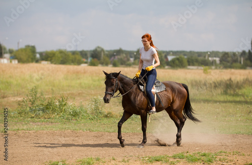 A redhead woman in yellow gloves riding a horse in nature