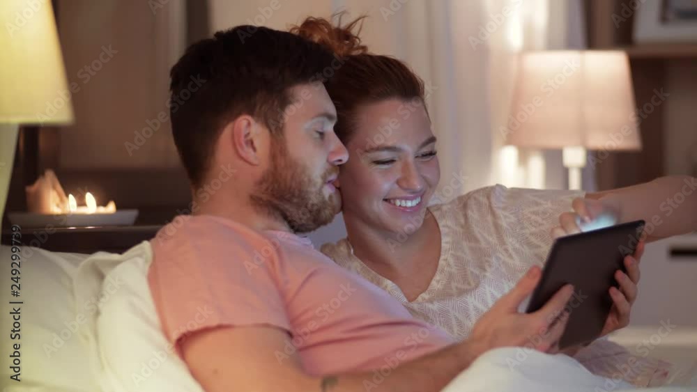technology, internet and communication concept - happy couple using tablet computer in bed at night technology, internet and communication concept - happy couple using tablet computer in bed at night