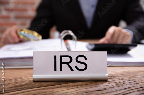 Photos Nameplate With IRS Title Kept On Businessman Desk