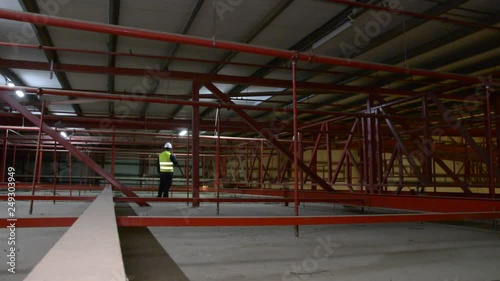 Technician engineer in a helmet checks the sprinklers pipes and roof constructions with a tablet