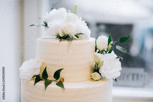 Beautiful and tasty white wedding cake at wedding reception with fresh flowers