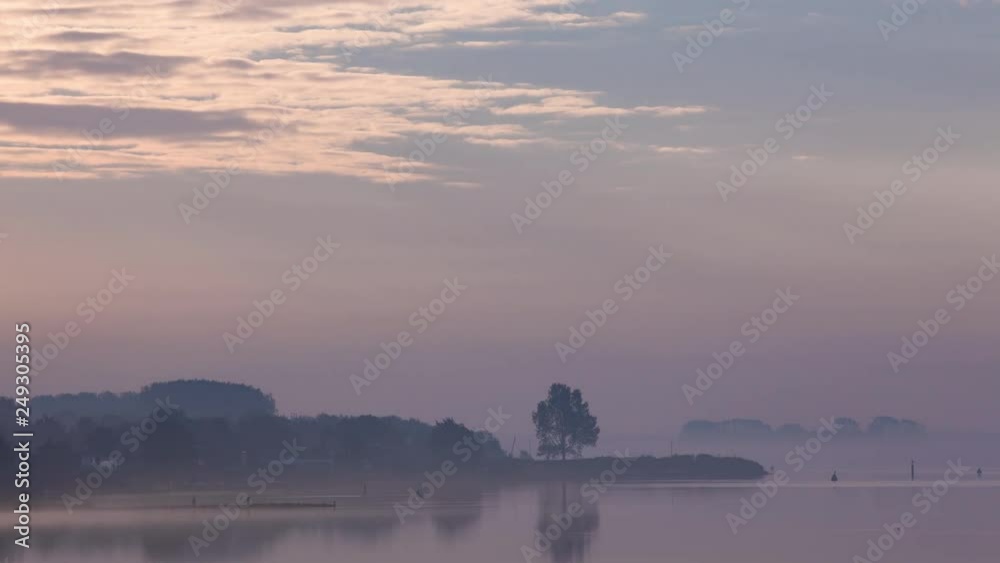Time lapse on a misty morning at the lake with some silhouettes of landscapes and a few light clouds coming from the left Time lapse on a misty morning at the lake with some silhouettes of landscapes and a few light clouds coming from the left