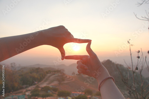 woman hands making frame gesture with sunrise on mountain background.