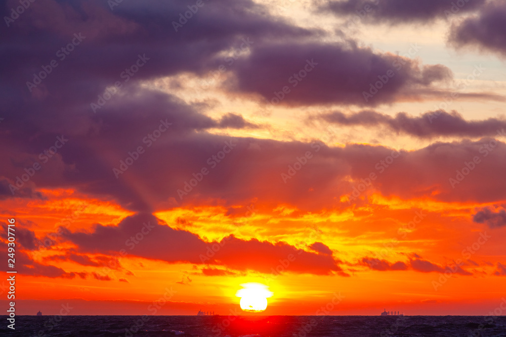 Obraz premium bright orange sun in a cloudy sky over the sea during sunset