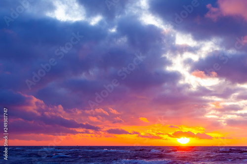 bright orange sun in a cloudy sky over the sea during sunset