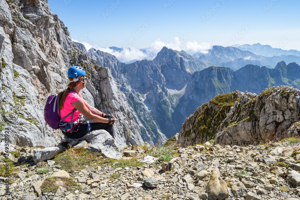 Young girl enjoying the views from a peak in Julian Alps, Triglav National Park, Slovenia, during a break on a via ferrata route, on a hot, bright, Summer day