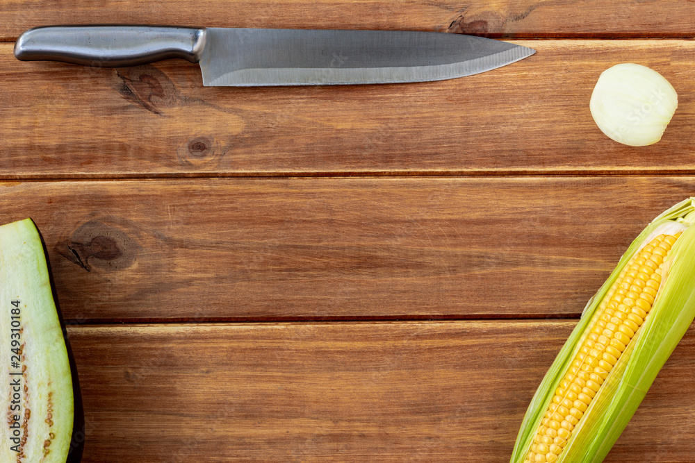 A silver metal knife next to some vegetables on a rustic wooden table. Free space for writing. Top view of the table A silver metal knife next to some vegetables on a rustic wooden table. Free space for writing. Top view of the table