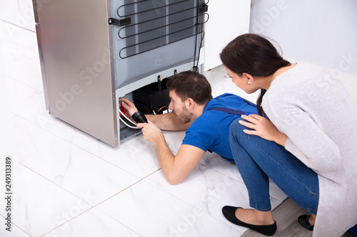 Technician Examining Refrigerator With Flashlight