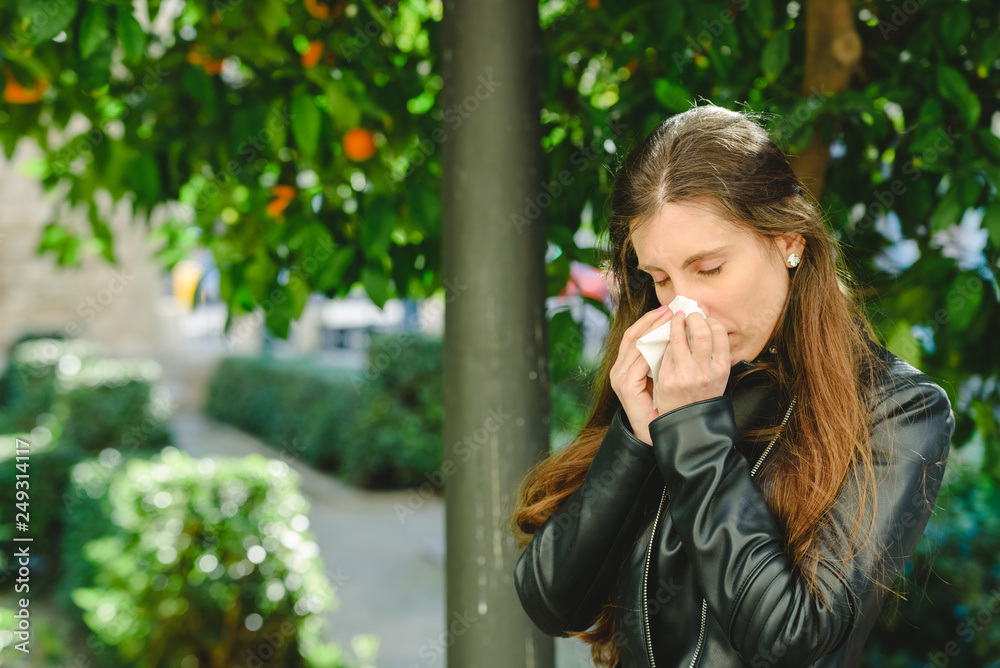 Brown-haired woman using a tissue to blow her nose and clean her nose of a cold.