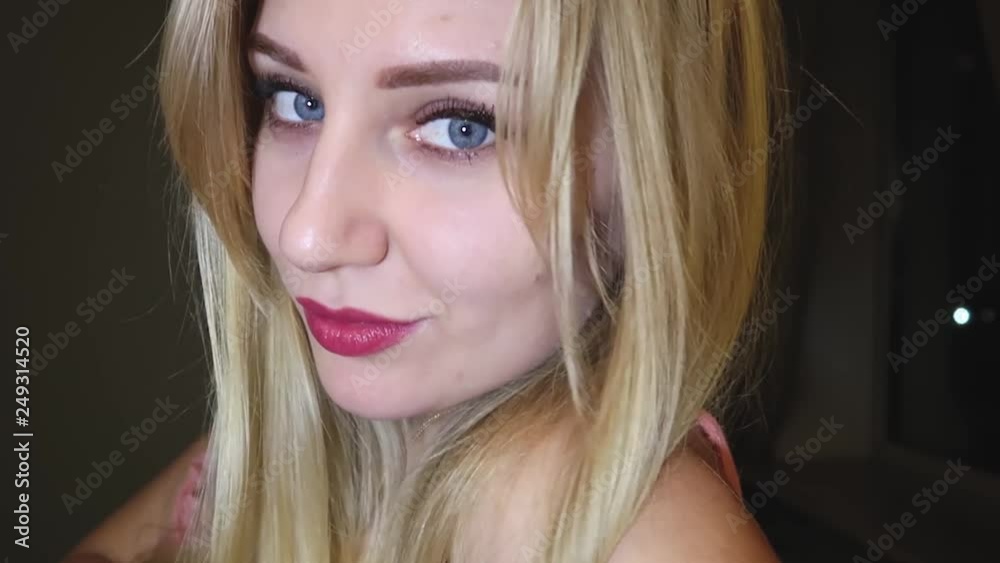 beautiful young blond woman with bright blue eyes and red plump lips flirts with the camera, flirting and smiling against a dark background, close-up portrait beautiful young blond woman with bright blue eyes and red plump lips flirts with the camera, flirting and smiling against a dark background, close-up portrait