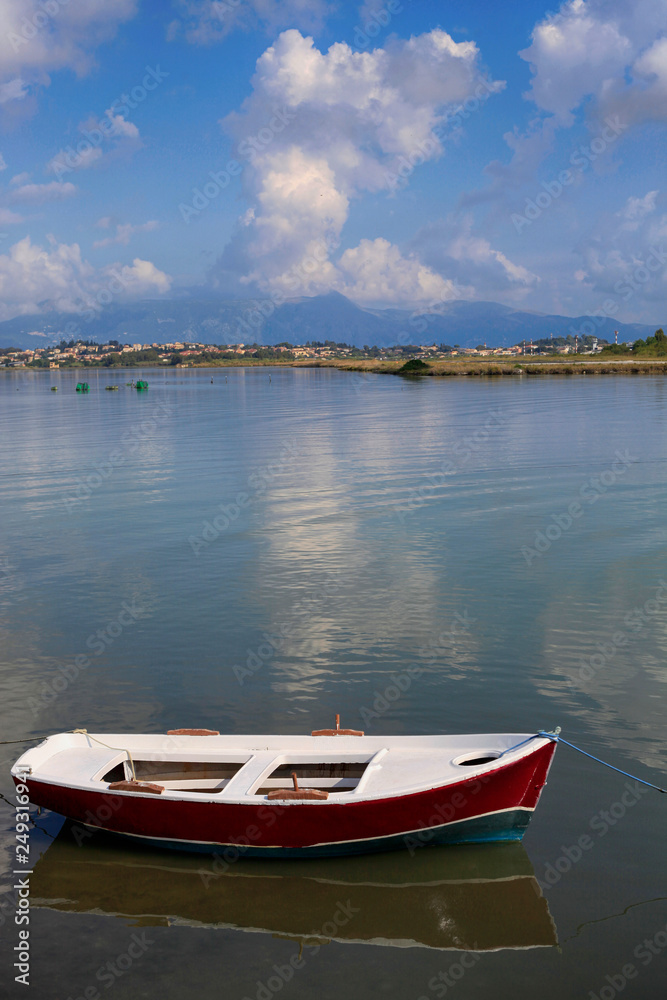 Summer landscape off the coast of Corfu island in Greece with a fishing boat in calm sea water, beautiful cloudy sky and mountains in the background